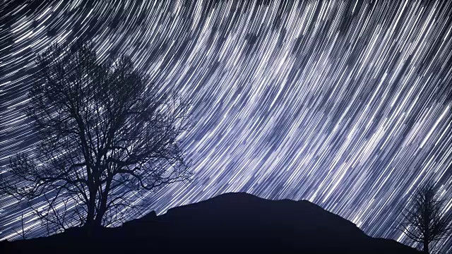 一个星光灿烂的夜晚，在前景中有一棵树的影子，并有星星的踪迹效果视频素材