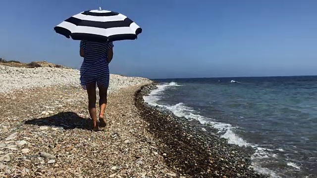 女人撑着伞在海边散步视频素材