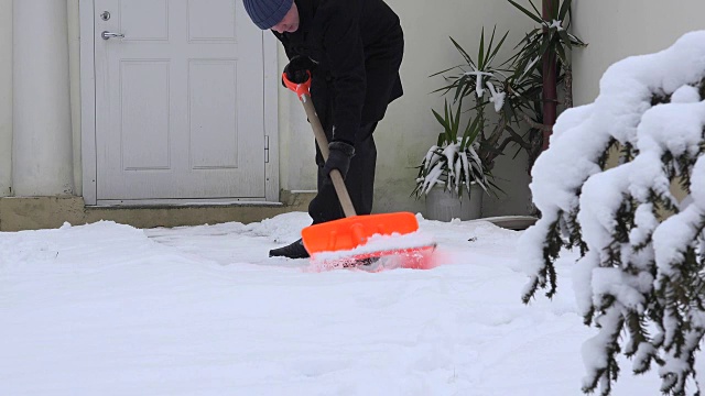 寒冷的冬天，男人用铁铲从家里清理积雪。FullHD视频素材