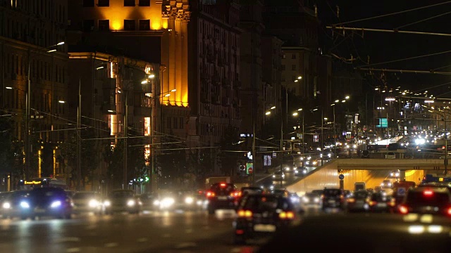 出租车经过夜晚的城市灯光，交通堵塞的隧道，十字路口，市中心在模糊。车头灯和led灯反射在隧道墙壁上。有轨电车的电线挂在电线杆上视频素材