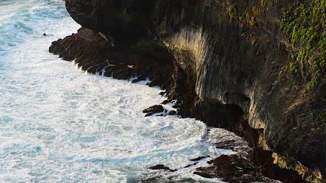 海浪撞击热带海滩上的岩石形成水花形状。岩石海滩上的巨浪。印度尼西亚巴厘岛著名的乌鲁瓦图寺庙。视频素材