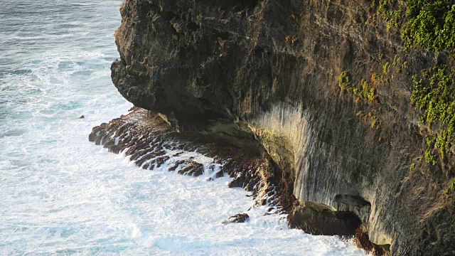 海浪撞击热带海滩上的岩石形成水花形状。岩石海滩上的巨浪。印度尼西亚巴厘岛著名的乌鲁瓦图寺庙。视频素材