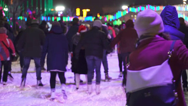 冬季运动概念。晚上在城市溜冰场的人群。一大群开心的人在滑冰。雪下降。圣诞天模糊。运动和好心情的概念。家庭和幸福的夫妇滑冰视频素材