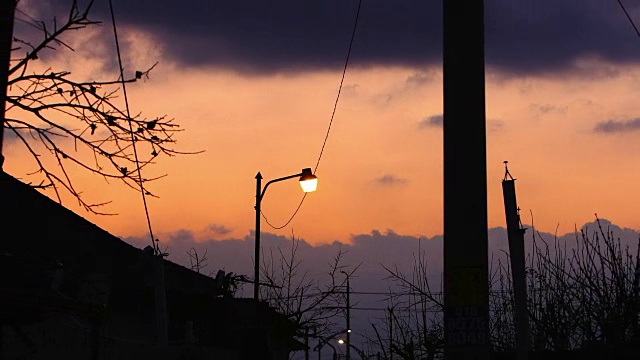 郊区的黄昏到夜晚的延时视图。街灯停留在移动的云与戏剧性的红色天空视频素材