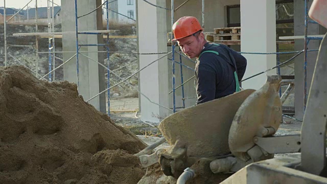 在建筑工地，一名白种人工人用铲子将沙子倒入混凝土搅拌机中视频素材