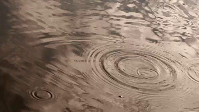 在雨季，近距离的雨水滴落在河面的金黄色调，4K Dci分辨率视频素材