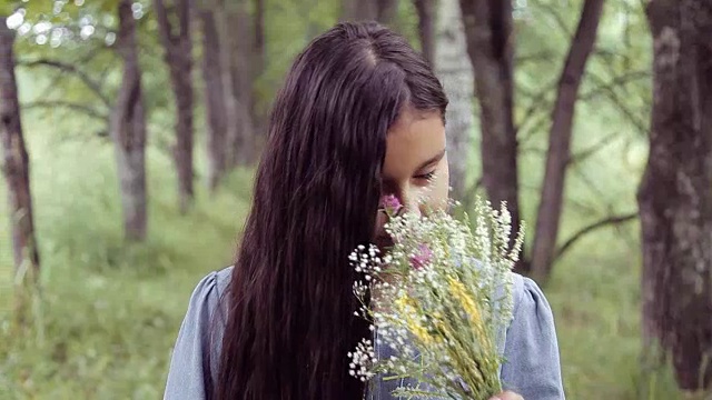 肖像。在一个阳光明媚的日子里，一个甜美美丽的小女孩站在大自然中嗅着一束鲜花，看着镜头幸福地微笑着视频素材