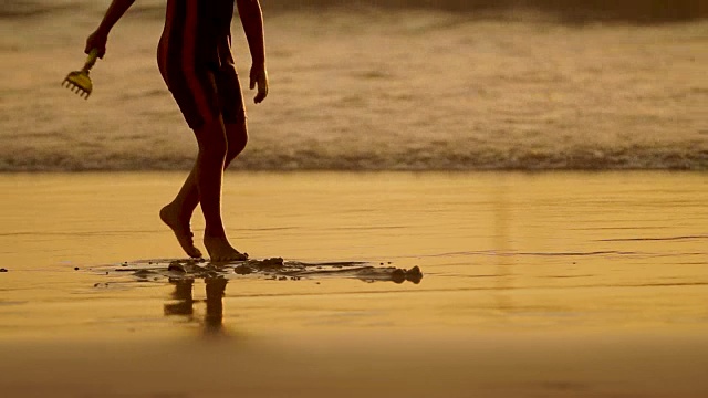 孩子在海浪中行走。孩子的脚在水里。夕阳在海浪中倒映。普吉岛,泰国视频素材