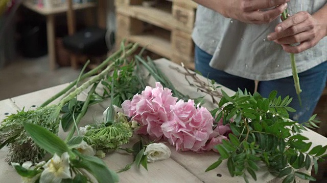 鲜花摊开在花店的木质柜台上，花商从柜台上拿起鲜花，开始制作4k的花束特写。视频素材