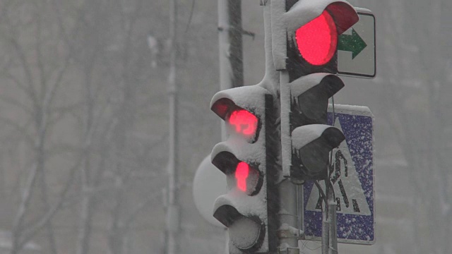 暴风雪期间，雪中的红绿灯控制交通。龙卷风来临时，大雪使道路上汽车的行驶变得复杂。特写镜头视频素材