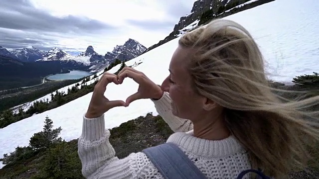 年轻女子在山湖上做心形手指架视频素材