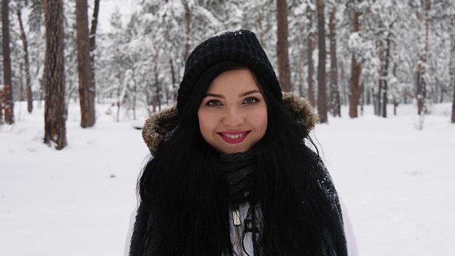 迷人的微笑褐发年轻女子在雪在森林。表达积极、真实的情感，享受下雪，等待圣诞假期视频素材