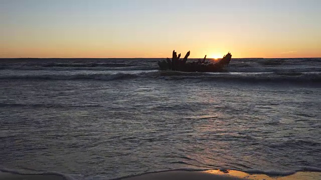 破旧的船在岸边失事，在暴风雨的海面和美丽的红色夕阳的背景下。波罗的海，爱沙尼亚，欧洲。视频下载