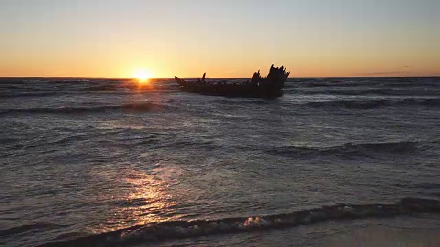 破旧的船在岸边失事，在暴风雨的海面和美丽的红色夕阳的背景下。波罗的海，爱沙尼亚，欧洲。视频下载