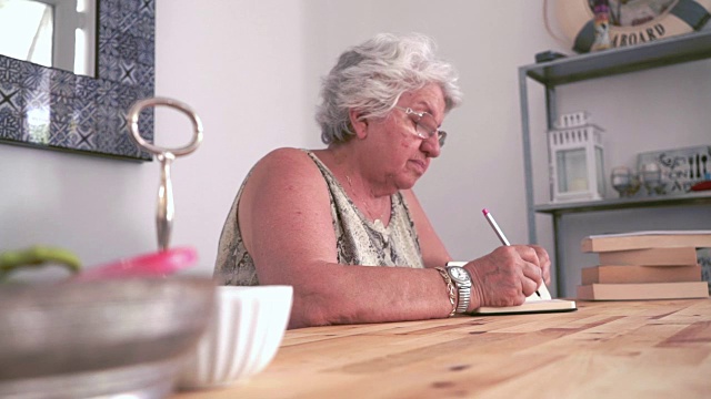 一位老妇人在笔记本上写字视频素材