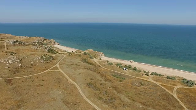 天线:蓝色海洋附近草原丘陵地带的乡村道路视频素材