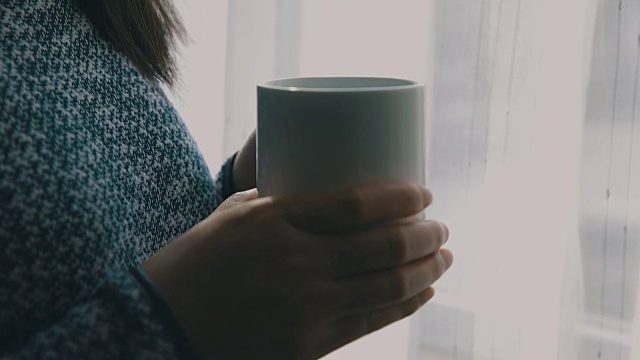 一个女人拿着咖啡靠近窗户的特写视频素材