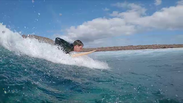 慢动作:年轻的冲浪者在冲浪板上划桨，抓住一个很酷的大浪。视频素材