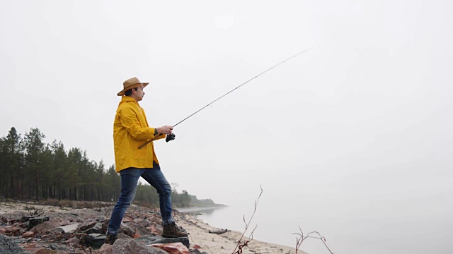 身穿黄色雨衣的渔民用慢动作抛出带有旋转杆的渔具视频素材