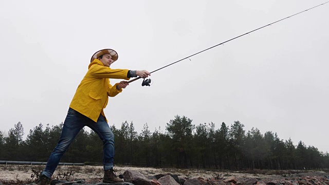 身穿黄色雨衣的渔民用慢动作抛出带有旋转杆的渔具视频素材