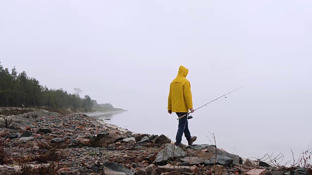 穿着黄色雨衣的渔夫沿着旋转的道路来到海岸，望着大海视频素材