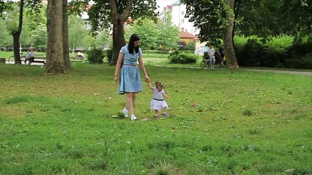 在妈妈的帮助下，女婴正在迈出她的第一步。可爱的小女孩跟着妈妈学走路视频素材