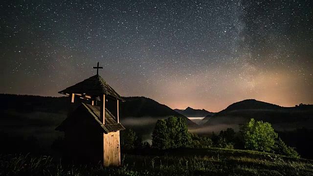 星星和银河移动在木制钟楼在山区和雾谷乡村。多莉拍摄时间流逝的星空视频素材