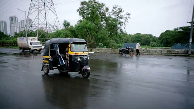 一名男子在下雨的孟买街道上驾驶三轮车。视频素材