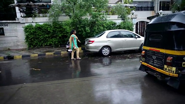 三轮车驶过，乘客在下雨的孟买街道上对着镜头吐舌头。视频素材