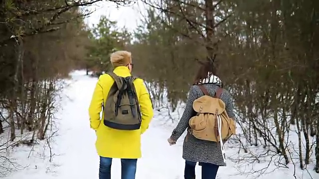 两个快乐的女人背着背包在冬天的森林里行走。视频素材