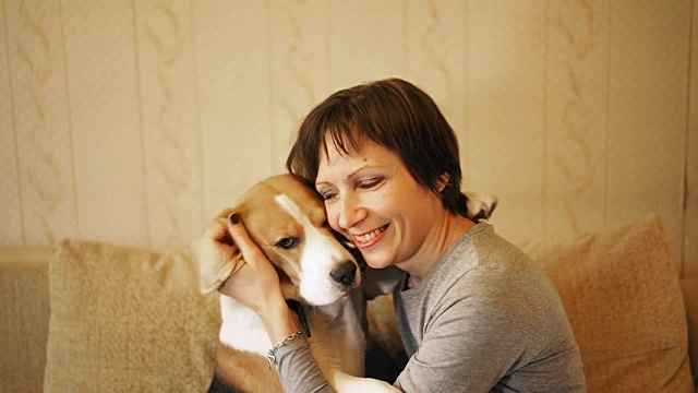 一个女人坐在沙发上，抱着一只小猎犬视频素材