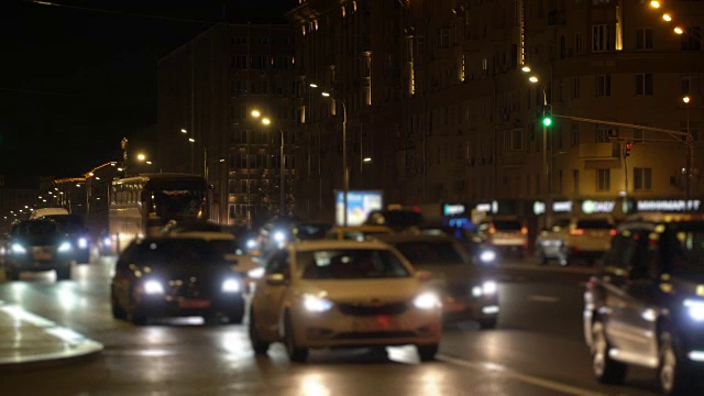 出租车经过夜晚的城市灯光，十字路口塞车，市中心一片模糊。车头灯和led灯反射在道路上视频素材