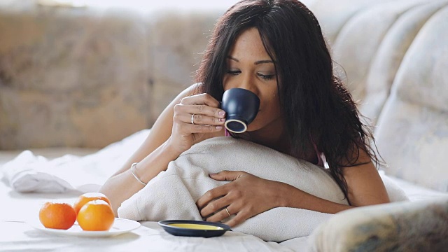 黑发女人在舒适的床上喝着茶在家视频素材