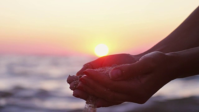 女性的手倒海沙通过她的手指在日落与镜头光晕效果的海洋背景。缓慢的运动。1920 x1080视频素材