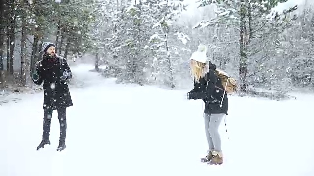 无忧无虑的快乐的年轻夫妇一起在雪地里玩，在冬天的林地里互相扔雪球在一个模拟战斗视频素材