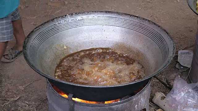 在临时的火坑上，一名男子将鱼放入热油锅中烹饪(近距离)视频素材