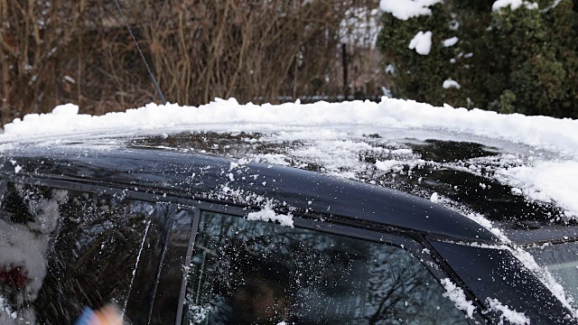 年轻人正在用刷子清理车上的雪。视频素材