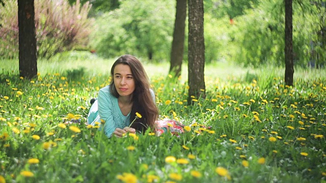 《草地上的美女》美丽的年轻女孩户外。享受大自然。健康微笑的女孩躺在绿草和野花。笑和快乐视频素材