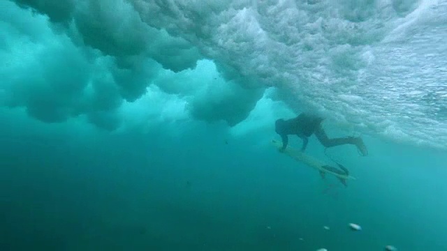 水下:男性冲浪者在深水中划桨，狂暴的海浪在他上面撞击。视频素材