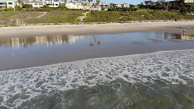 航拍从水晶清澈的海洋，经过一群冲浪者，到沙滩和悬崖在远处的盐溪海滩在拉古纳，橘子县，加州。视频素材