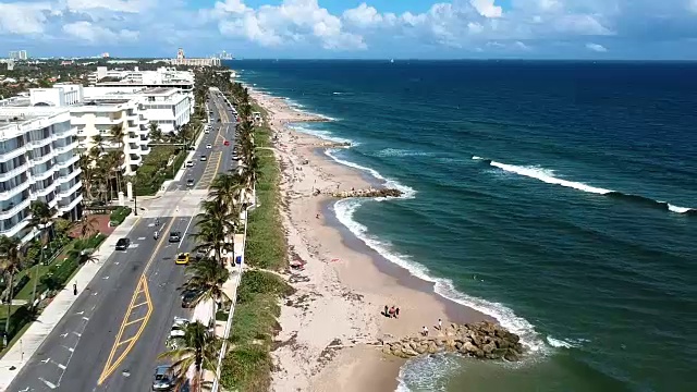 美丽的航拍向后飞行在佛罗里达棕榈滩与海滩街道，海浪，多云的天空，棕榈树，和度假胜地视频素材