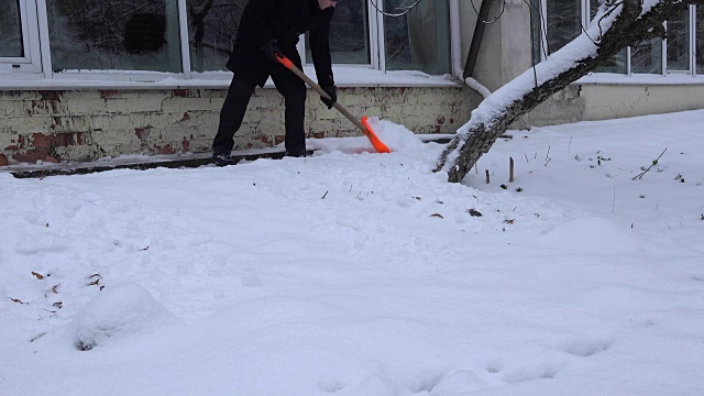 冬天，人们用铁锹清理房子墙附近的积雪。FullHD视频素材