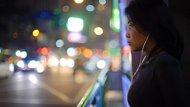 亚洲女人听音乐通过耳机在夜晚的城市视频素材