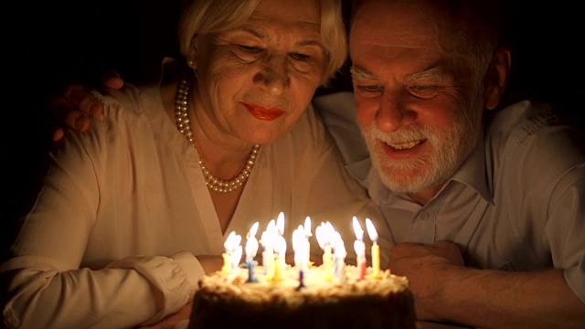 相爱的老年夫妇晚上在家用蛋糕庆祝结婚纪念日。吹灭蜡烛视频素材