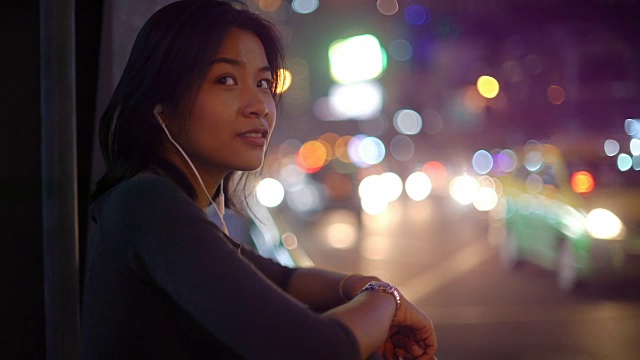 亚洲女人使用智能手机与耳机在夜晚的城市视频素材