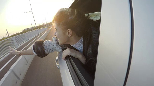 快乐迷人的女人在夕阳西下时，在汽车的后座上愉快地挥手，她的头伸出窗外视频素材