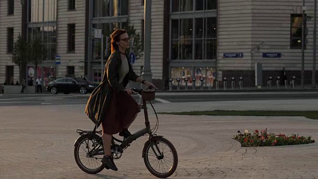 年轻的红发女子骑着自行车在街道上的背景汽车行驶在道路上视频素材