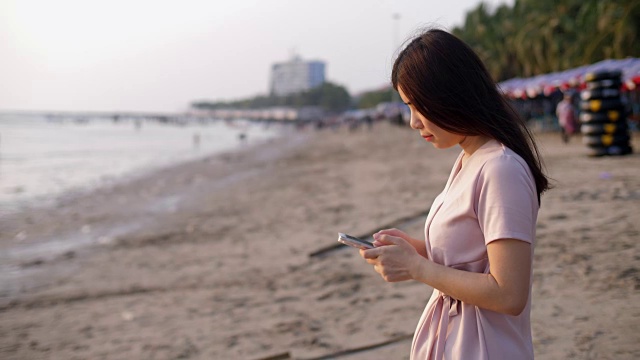 有魅力的女人在海滩上用手机发短信视频素材