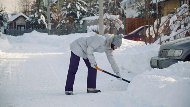 冬天，年轻女子在郊区用铁铲为汽车清理积雪视频素材