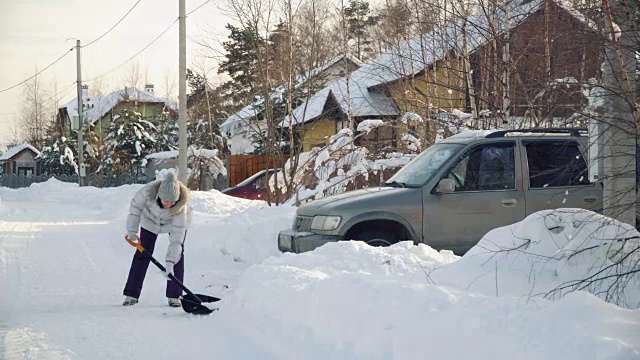 冬天，年轻女子在郊区用铁铲为汽车清理积雪视频素材